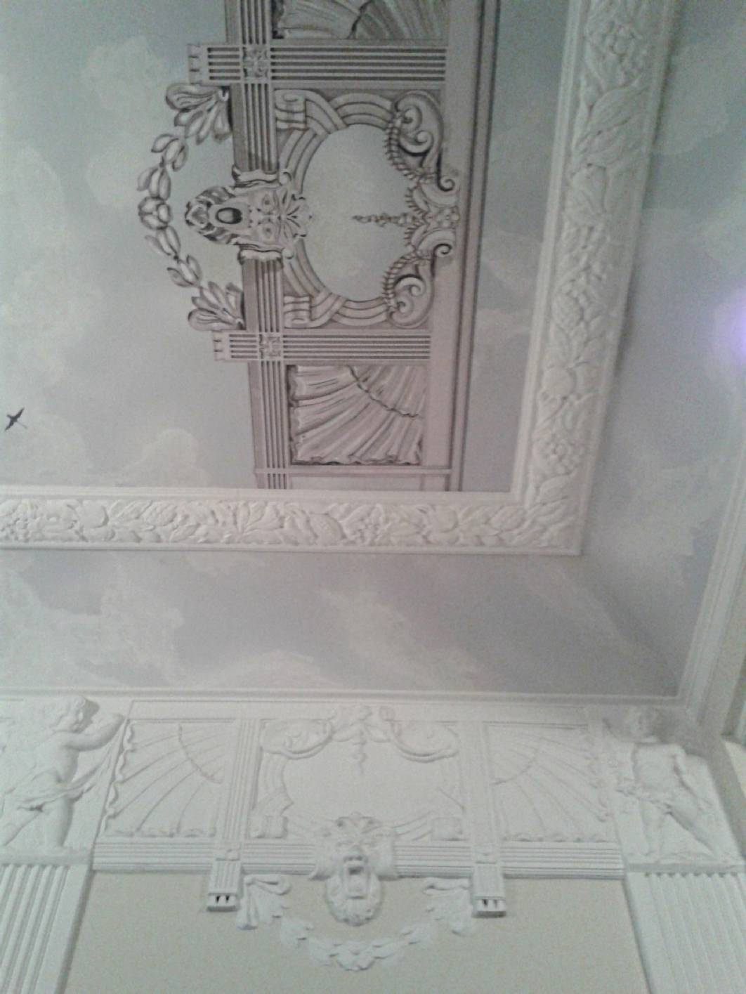 Kopie eines Stuck – Elementes als Deckenmalerei in einem Charlottenburger Treppenhaus aus dem Jugendstil. Die Deckenmalerei wurde als Graumalerei mit gemaltem Himmel in Lasurtechnik ausgeführt. Norbert Schimpf hat das Konzept für das Treppenhaus erstellt. Der Innungsbetrieb ist Experte für Exklusive Malerarbeiten und Restaurierung in Berlin.